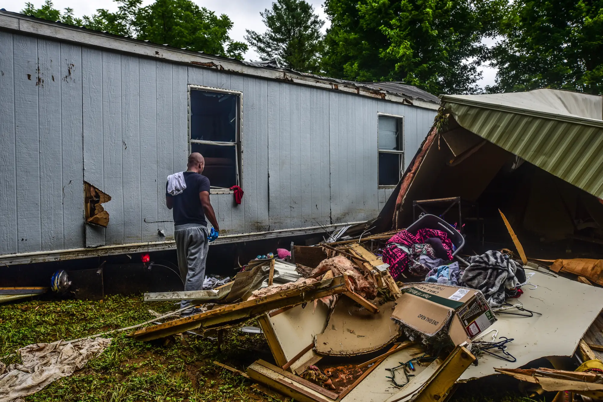 A man walking through rubble next to a mobile home